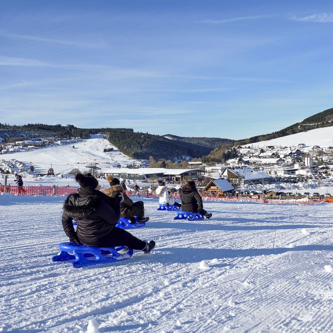 Erwachsene rodeln an der Dorfwiese mit Blick auf Willingen 