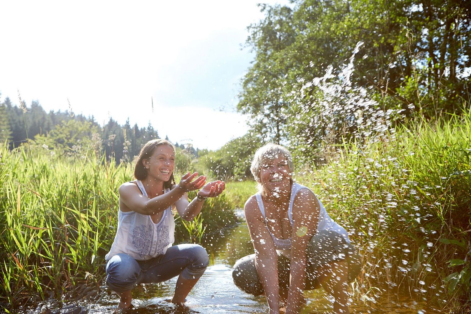 2 Frauen planschen im Sommer in einem Bach 