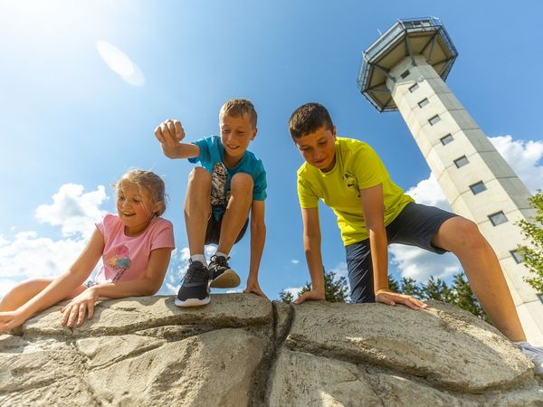 3 Kinder klettern auf einem Stein vor dem Hochheideturm in Willingen