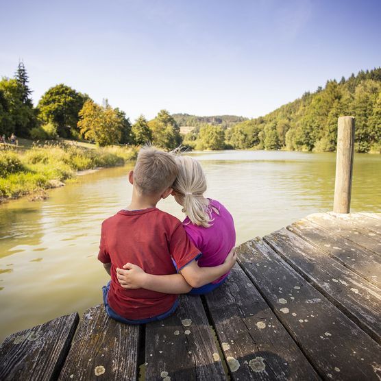 Kinderpaar Arm in Arm auf einem Steg am See